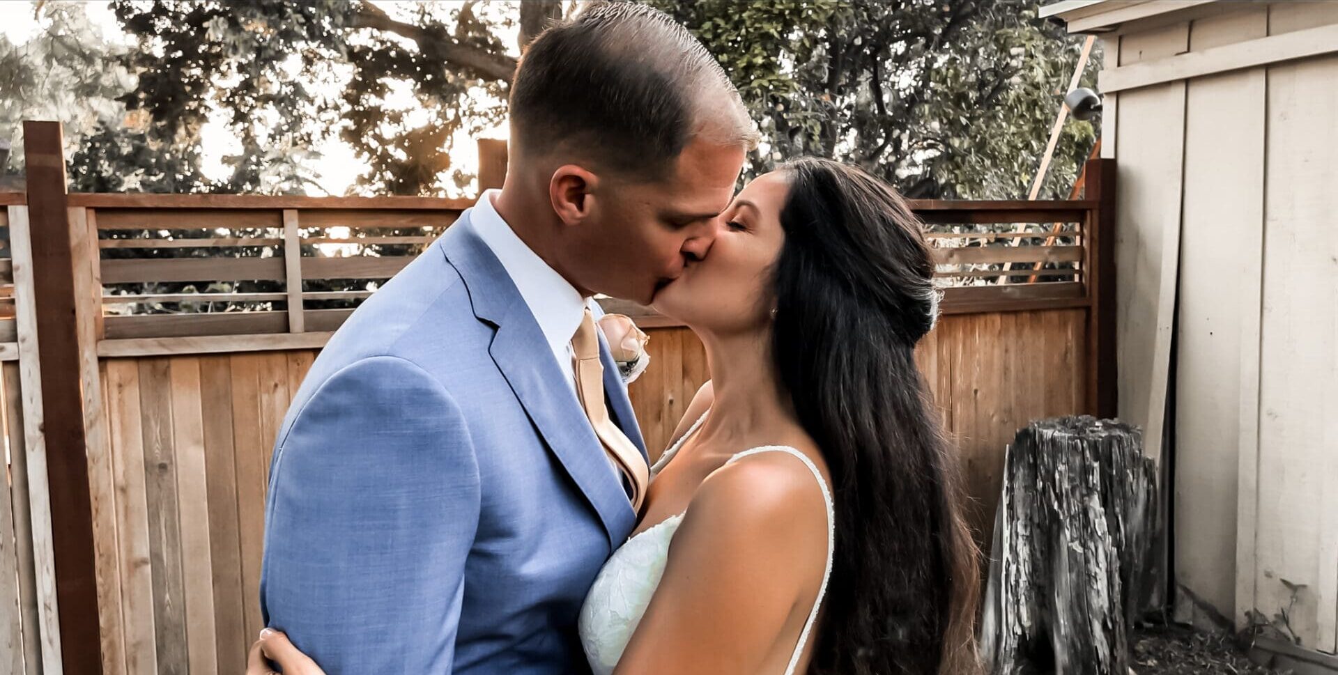 A man and woman kissing in front of a fence.